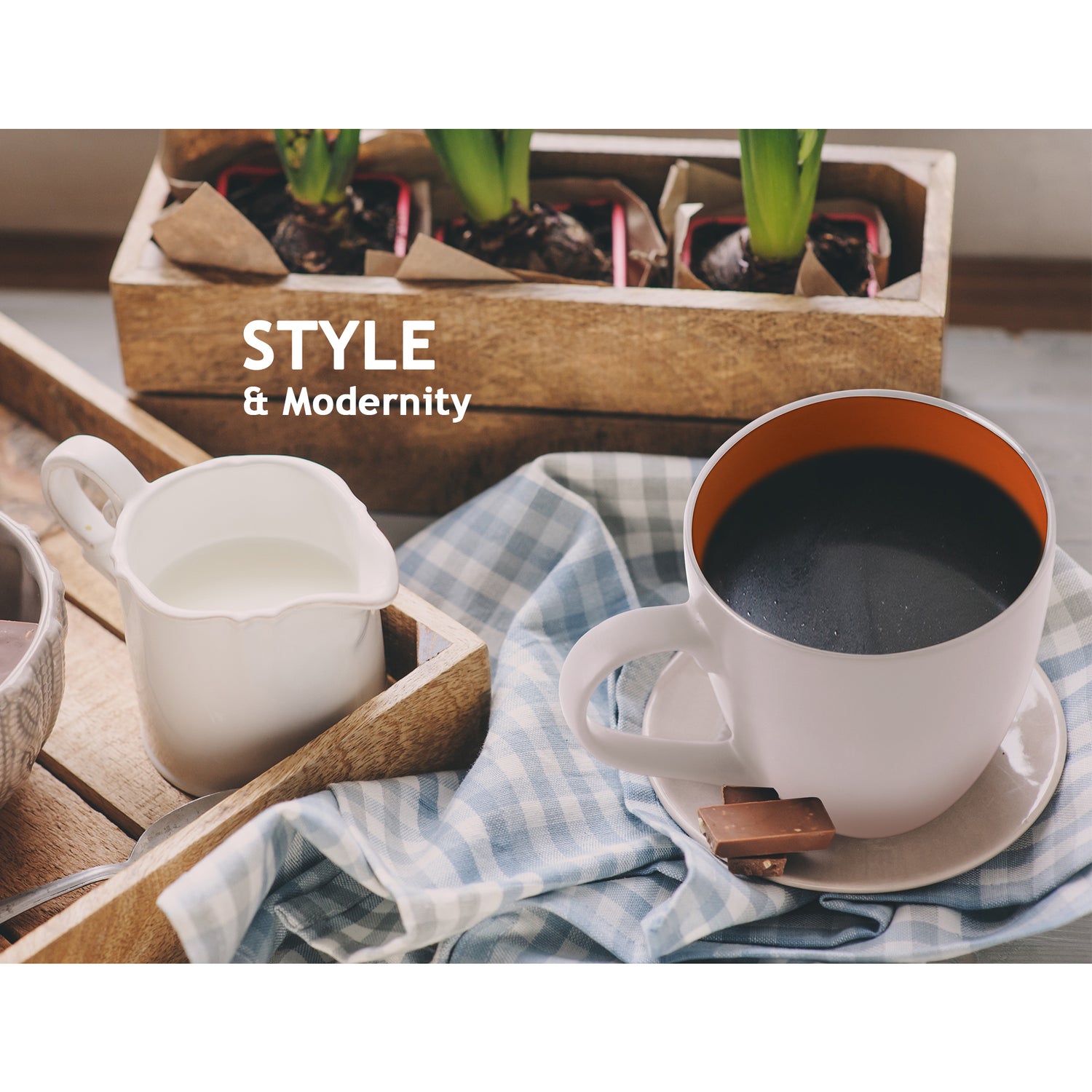Weiße Tasse der MIAMIO Le Papillon Kollektion neben einem Holztablett mit einer Kanne Milch und Blumen im Hintergrund