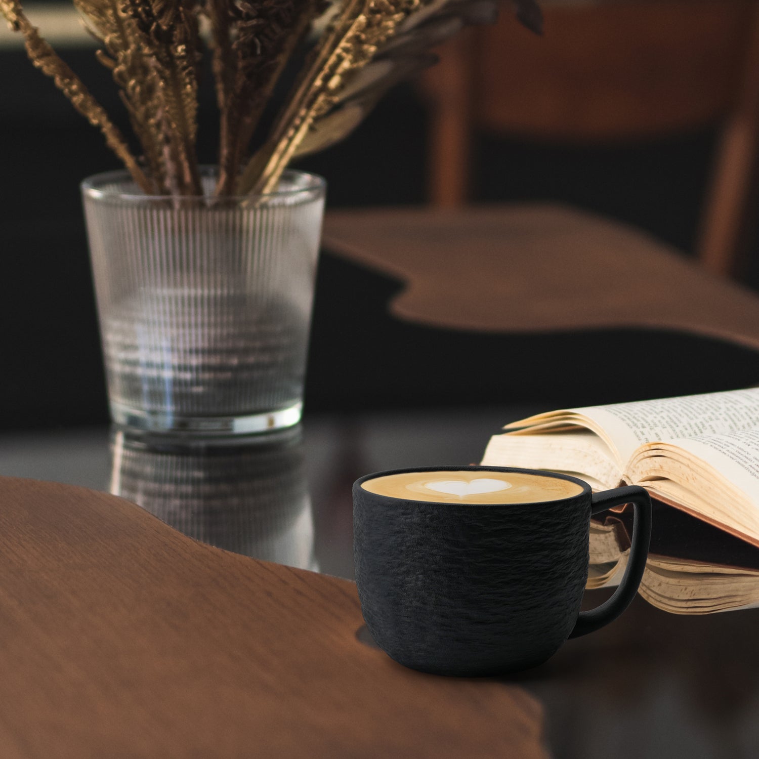 Schön angerichteter Cappuccino in einer Kaffeetasse von MIAMIO Oasis Kollektion neben einem geöffneten Buch und Pflanze im Hintergrund
