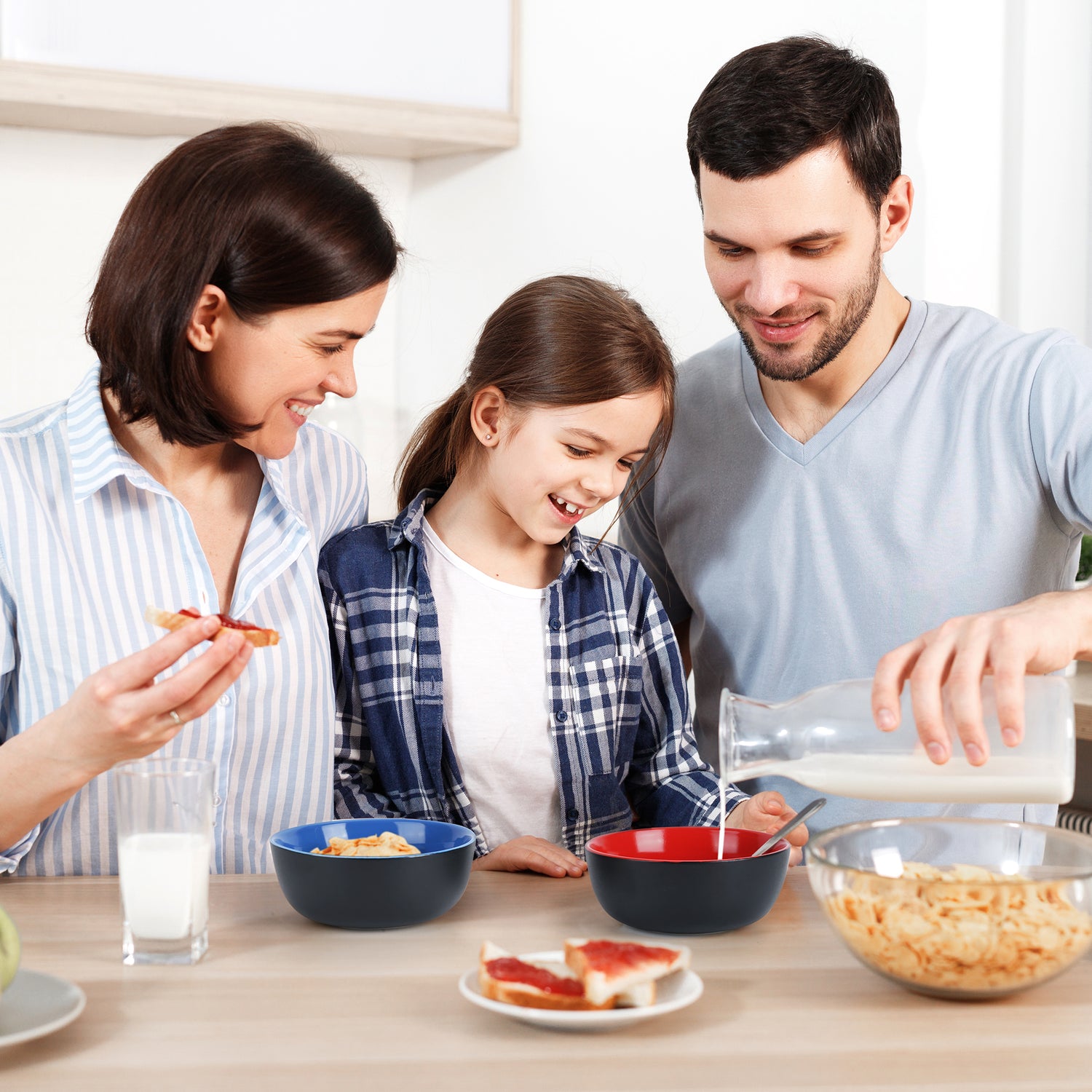 Eine glückliche Familie beim frühstücken wobei der Vater seiner Tochter Milch in die Schale einschenkt 