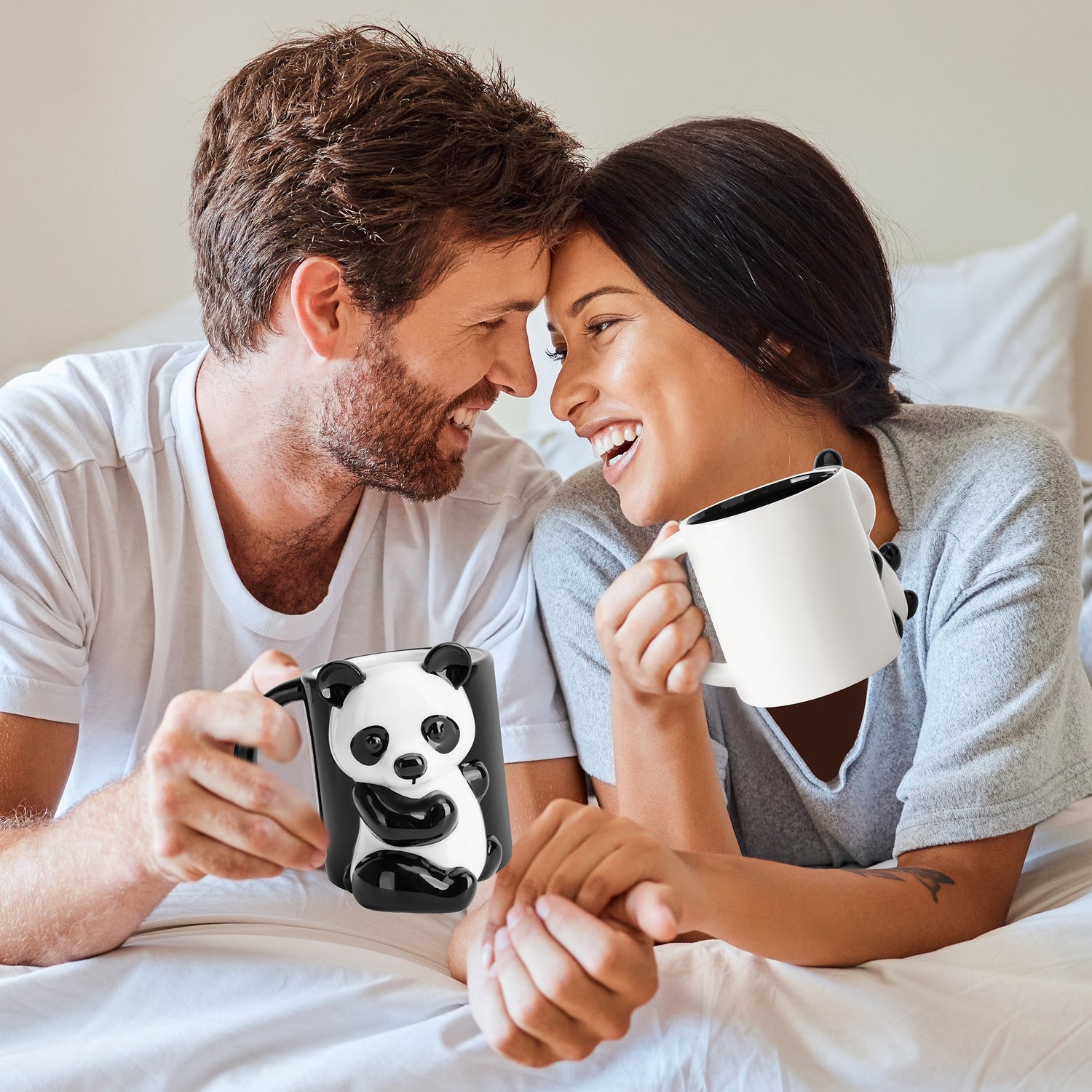 Lachendes und händehaltendes Pärchen im Bett mit MIAMIO Panda Tassen Set