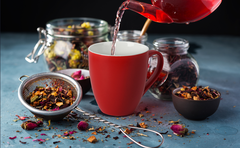 Rote MIAMIO Le Papillon Tasse mit Tee eingeschenkt und Kräuter in Schalen und Gläsern im Hintergrund
