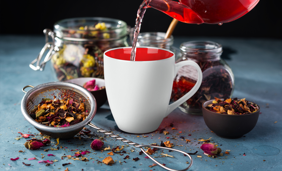Weiß rote MIAMIO Le Papillon Tasse mit Tee eingeschenkt und Kräuter in Schalen und Gläsern im Hintergrund